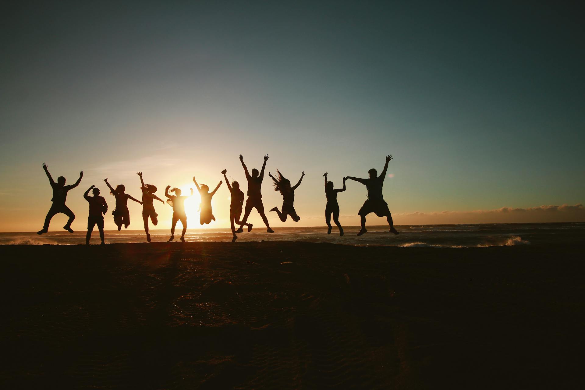 The group of people jumped simultaneously on the beach with direct sunlight toward them, creating a beautiful contrast and shadow.