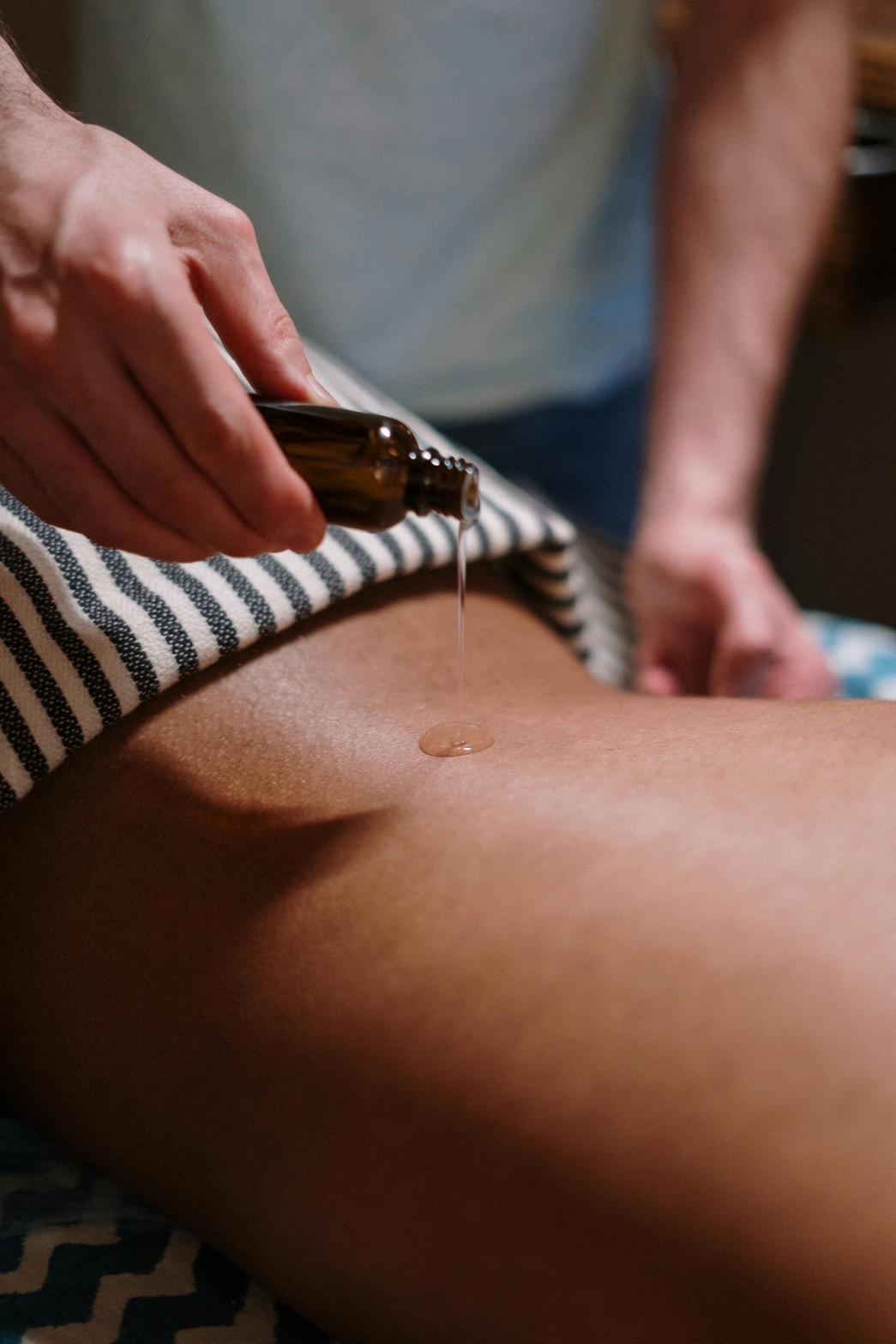 The skilful therapist is pouring essential oil on the client's back before performing an aromatherapy massage.