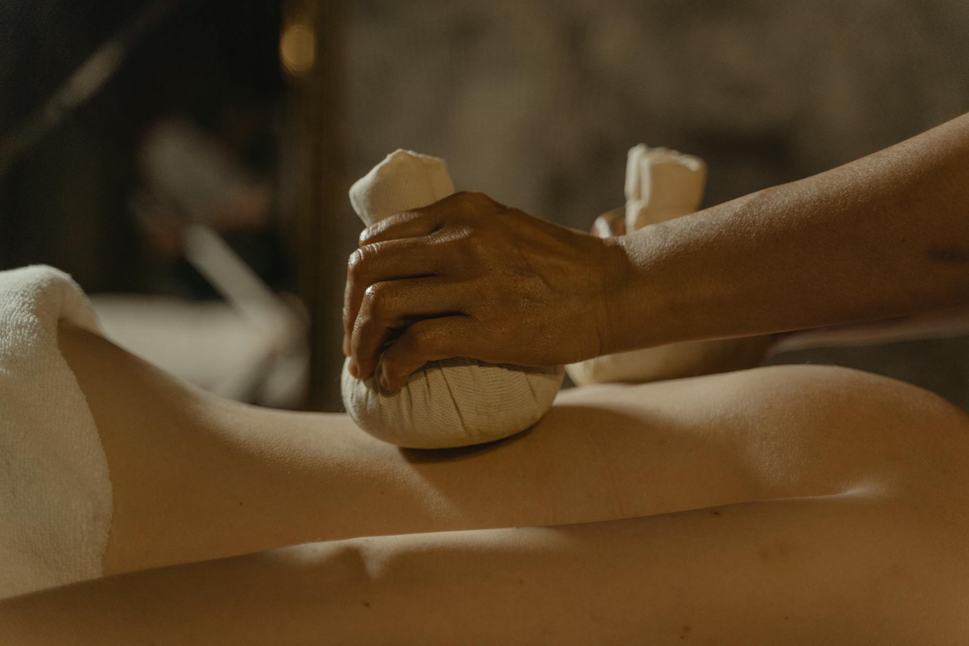 The therapist applies steamed herbal compresses filled with fragrant herbs to the client during the Thai Herbal Compress Massage session.